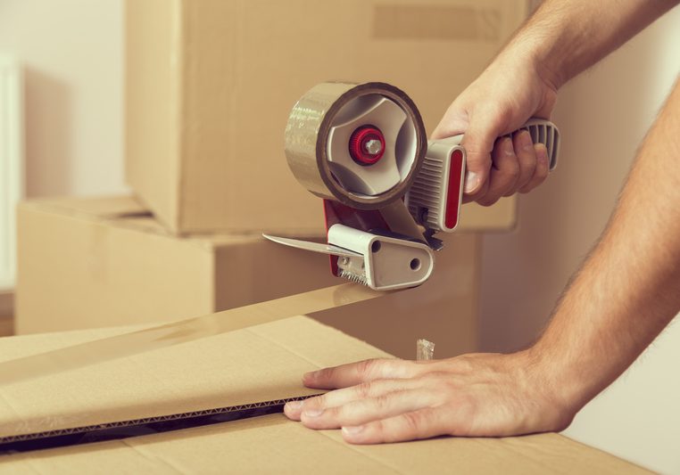 Close up of a guy s hands holding packing machine and sealing cardboard boxes with duct tape